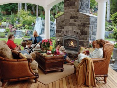A group of people are sitting around a fireplace on a patio