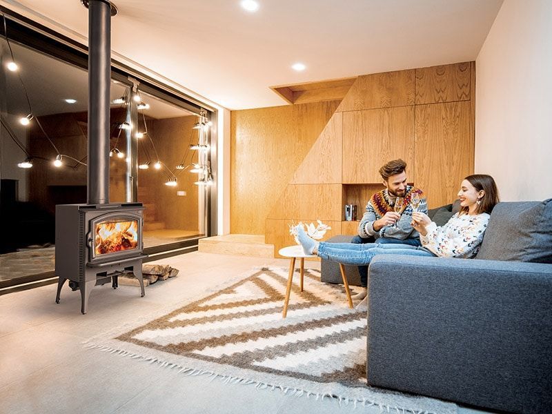 A man and a woman are sitting on a couch in a living room with a wood stove.