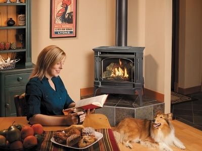 A woman is sitting at a table reading a book next to a dog.