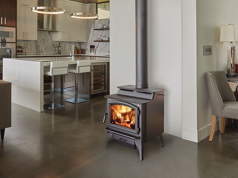 A wood stove is sitting in a living room next to a kitchen.