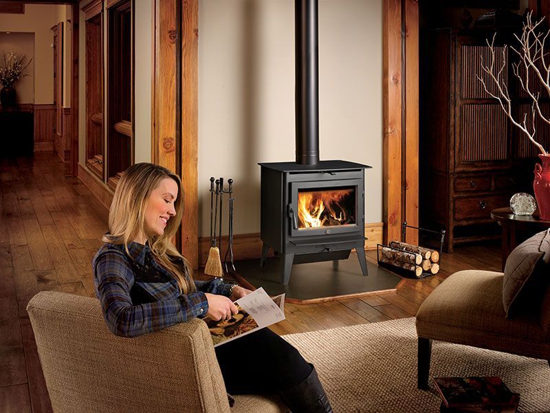 A woman is sitting in a chair in front of a wood stove in a living room.
