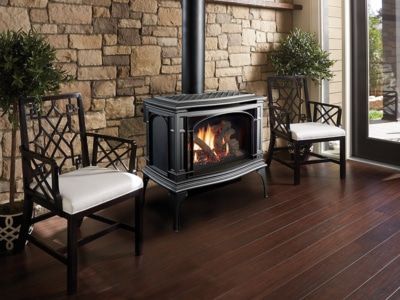 A wood stove is sitting in a living room next to two chairs.