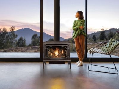 A woman is standing in front of a fireplace looking out a window.