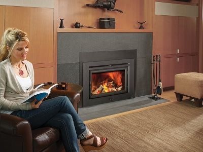 A woman is sitting in front of a fireplace reading a book.