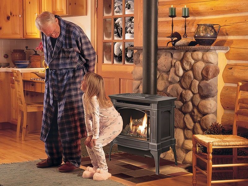 A man and a girl are looking at a wood stove in a log cabin.