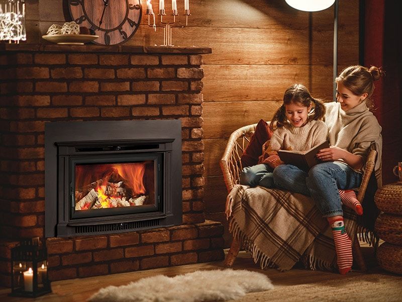 A woman and a child are sitting in front of a fireplace reading a book.