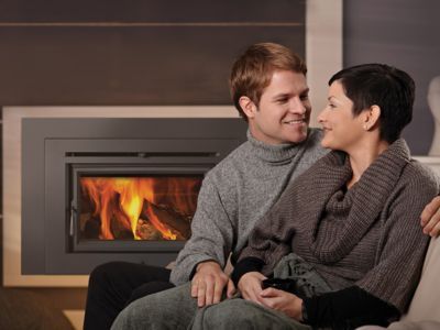 A man and a woman are sitting on a couch in front of a fireplace.