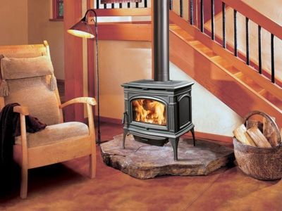 A wood stove in a living room next to a chair and stairs