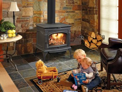 Two children are sitting on the floor reading a book in front of a wood stove.