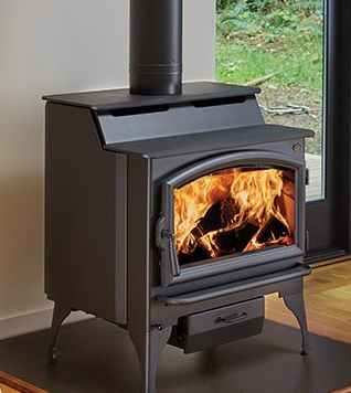 A wood stove is sitting on a wooden floor in front of a window.