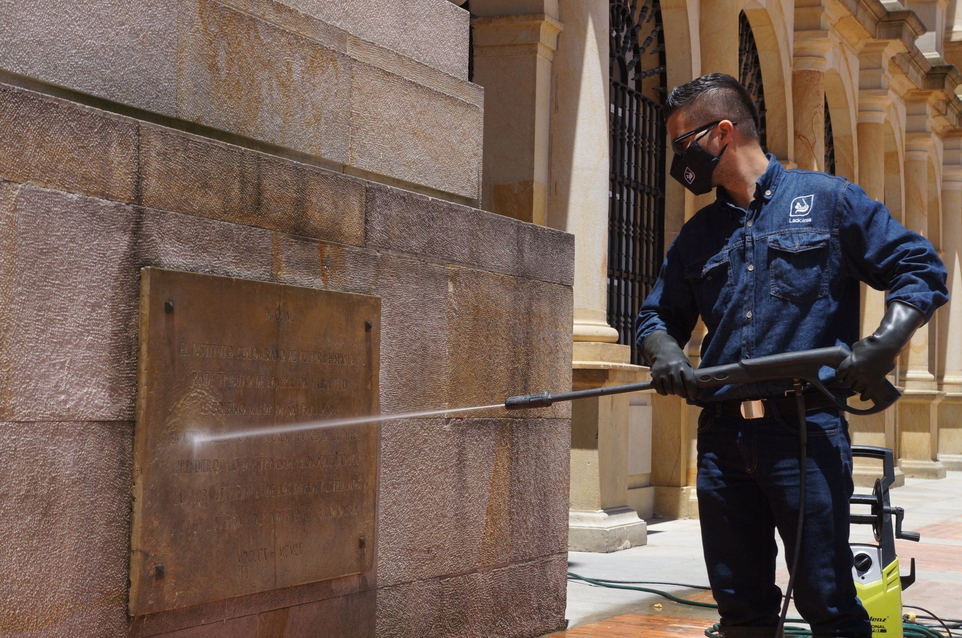 Un hombre que lleva una máscara está limpiando una pared de piedra con una lavadora de alta presión.