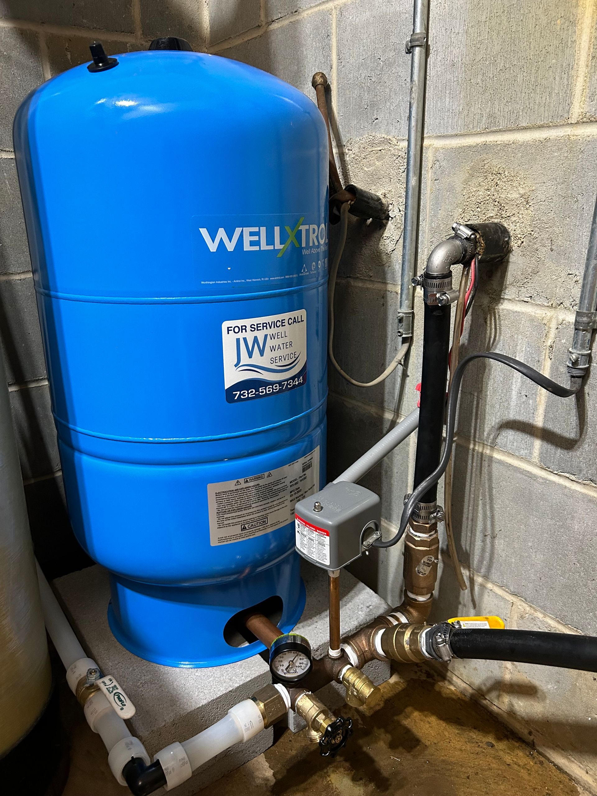 Blue water pressure tank with pipes and controls in a basement setting.