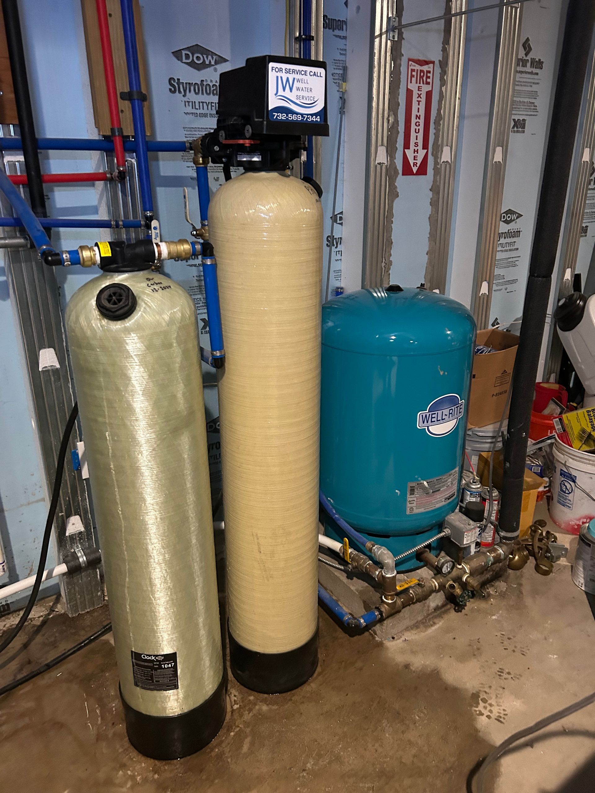 Water filtration system in a basement, with three tanks and piping.