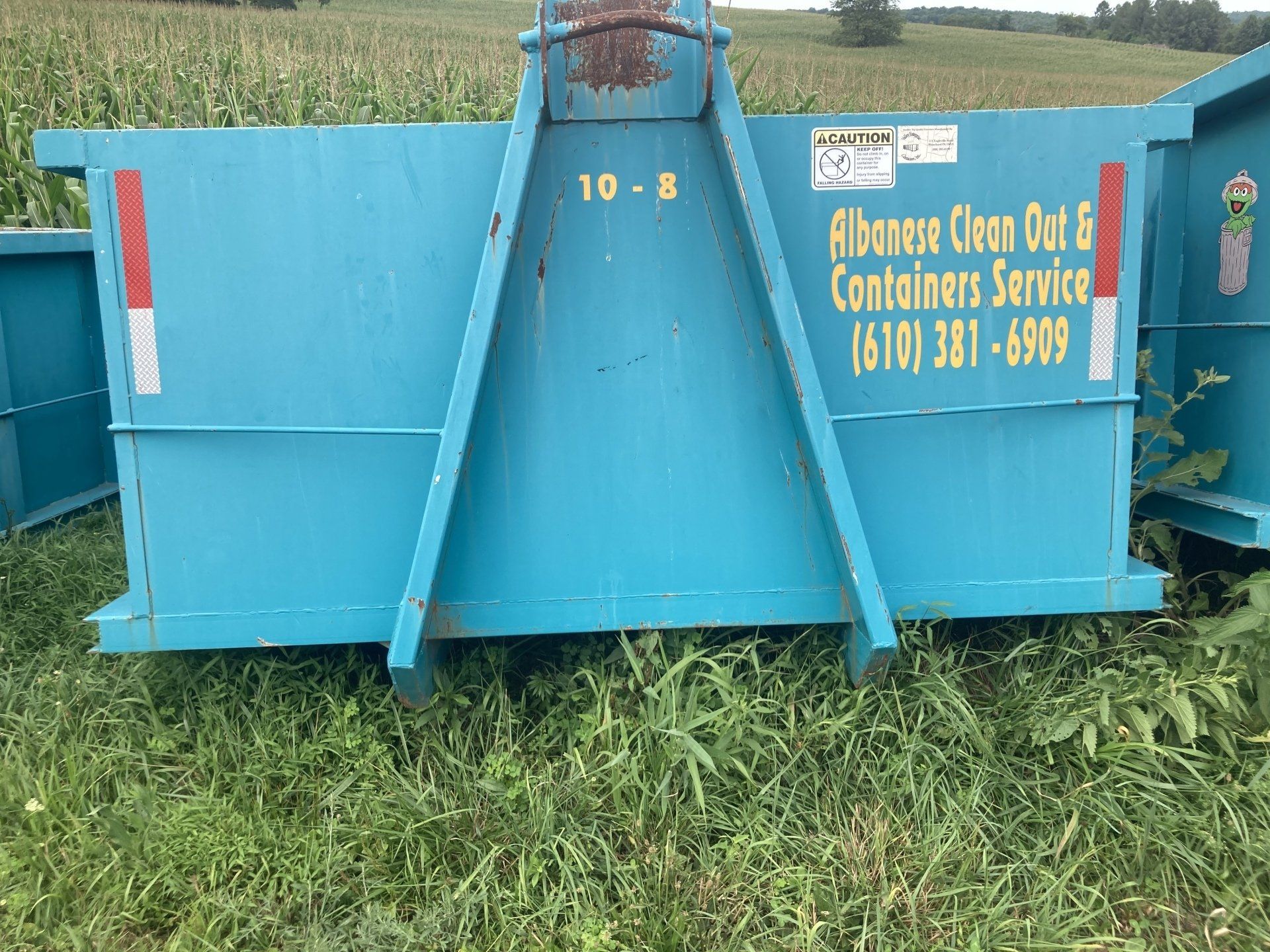A blue dumpster is sitting on top of a lush green field.