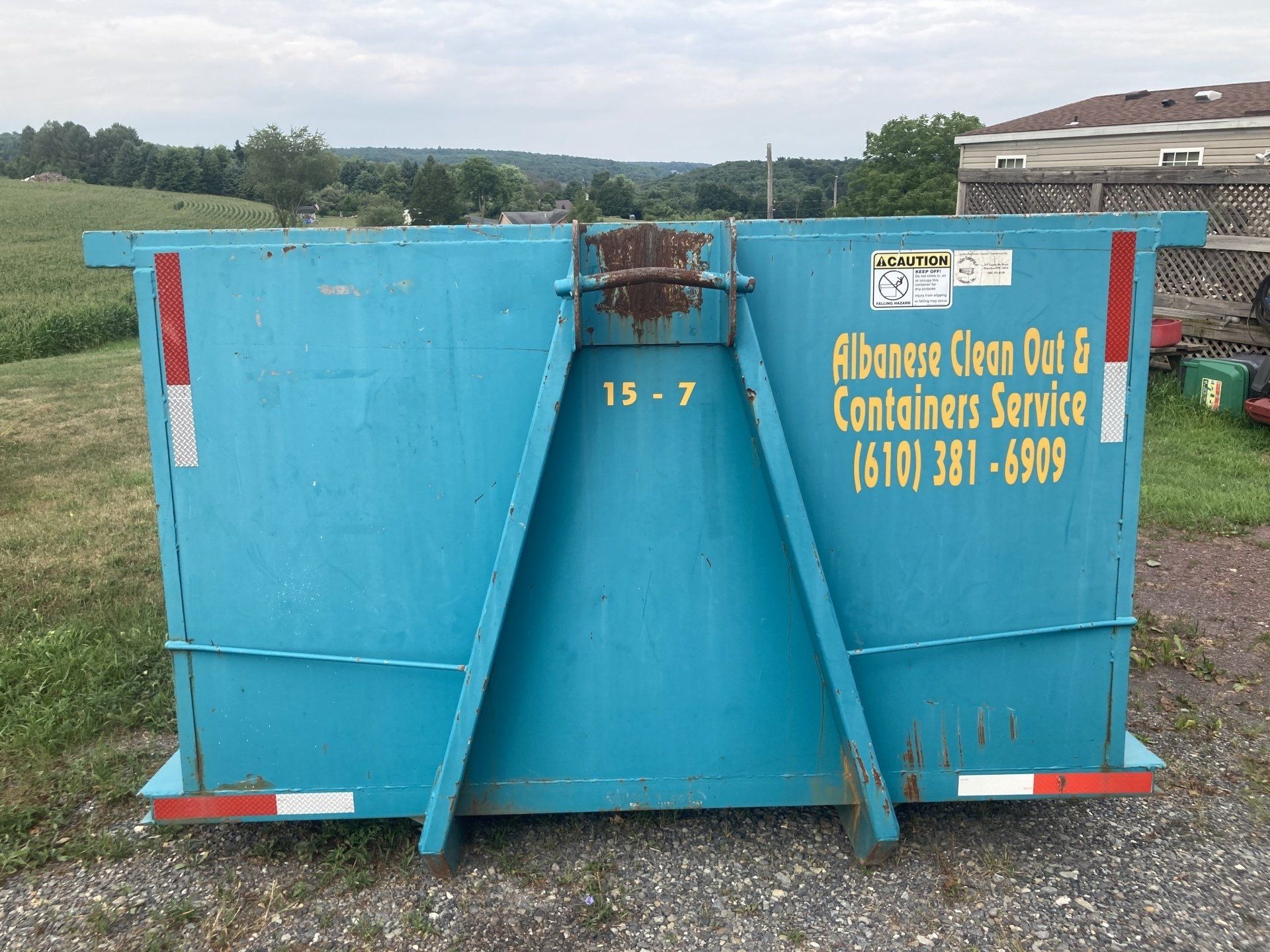 A blue dumpster is parked in a grassy field.