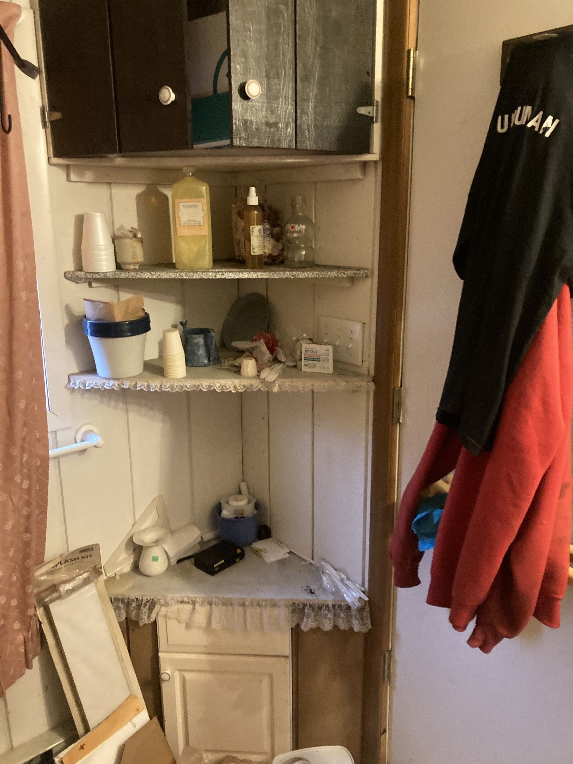 A corner of a room with shelves and a red jacket hanging on the wall