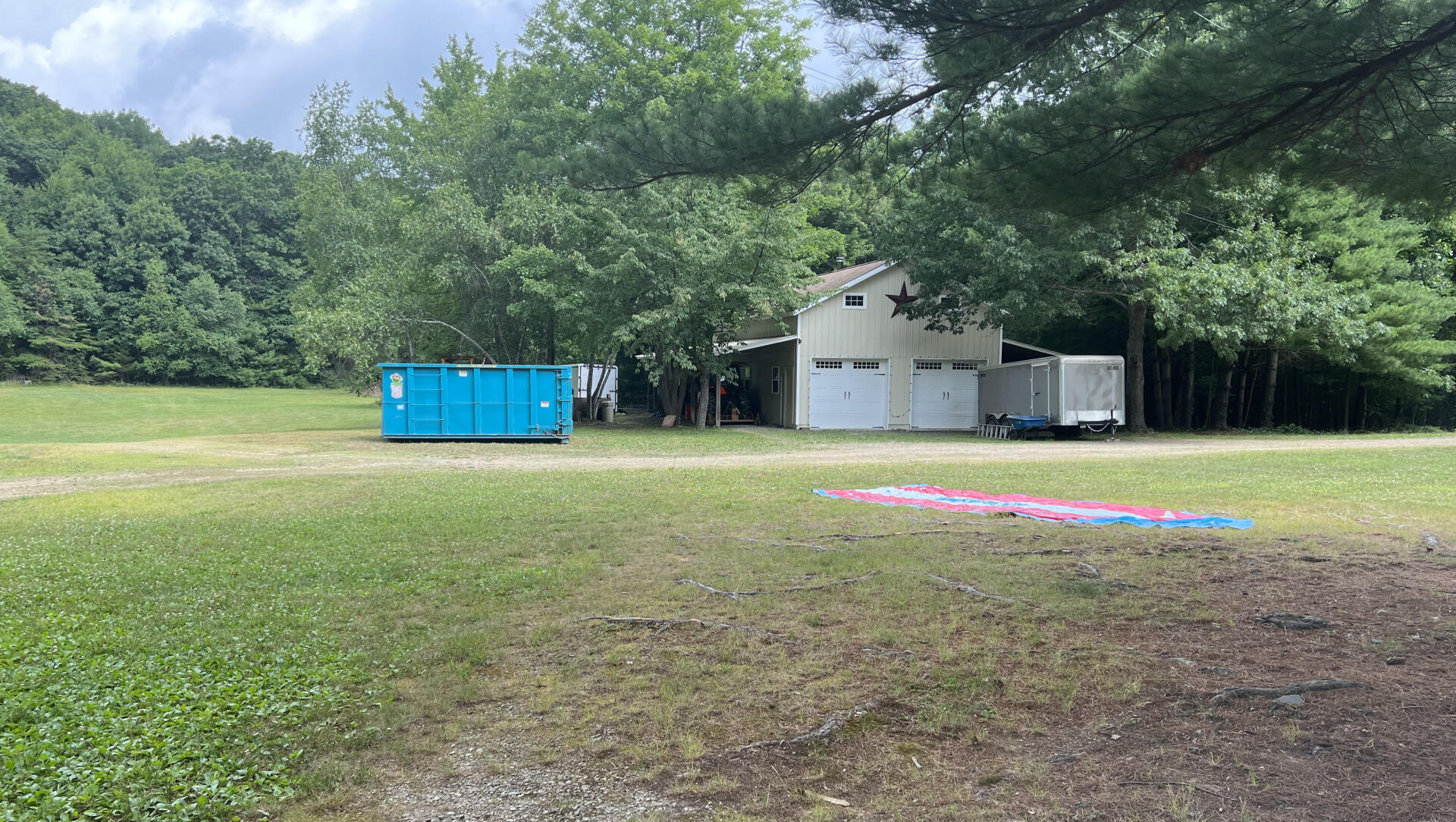 There is a blue dumpster in the middle of a grassy field.