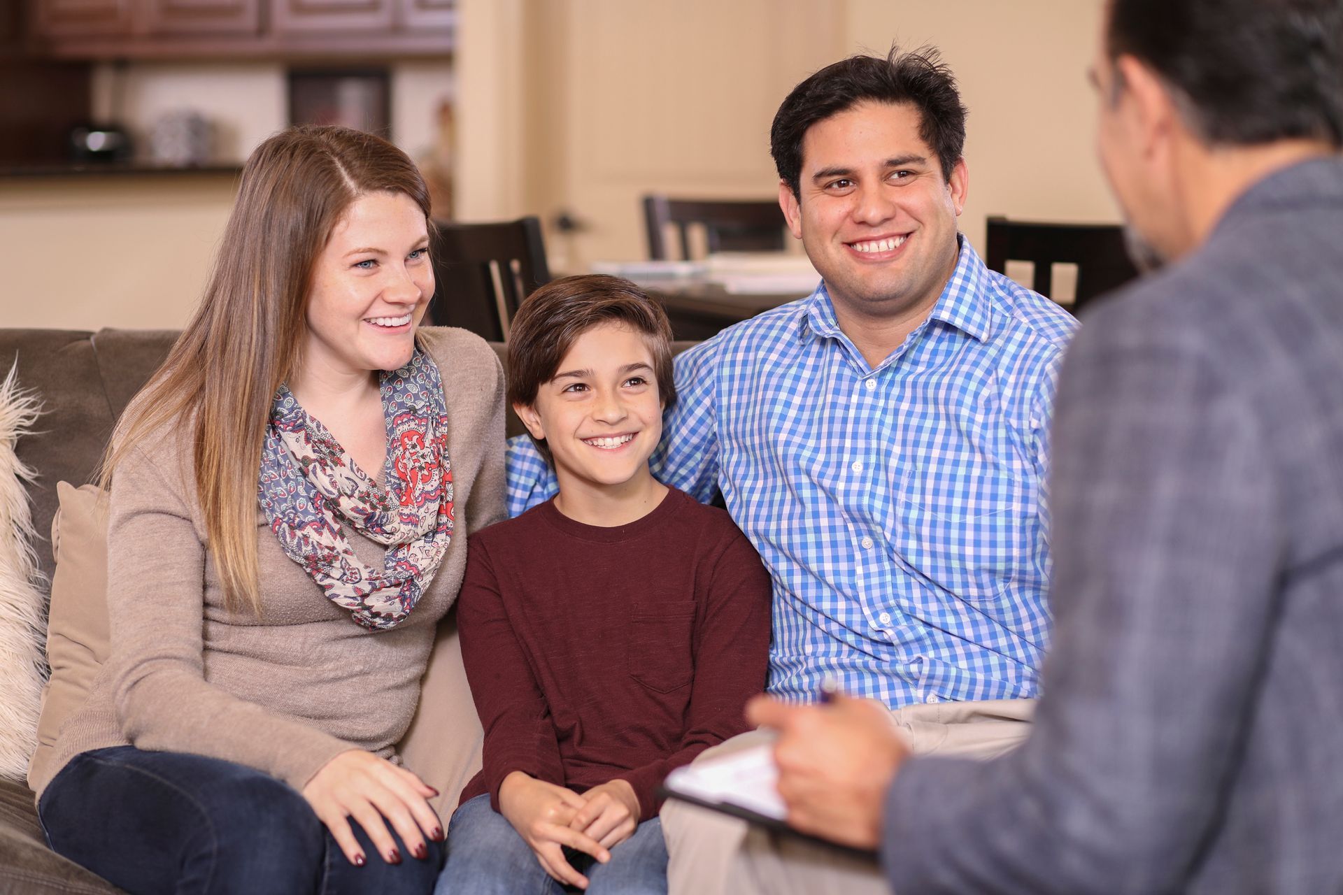 Family of three smiling, sitting on a couch, talking to a person holding a clipboard.