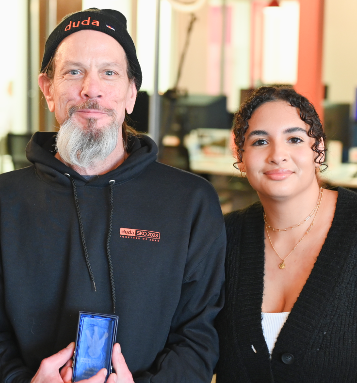 A man wearing a hat that says duda stands next to a woman