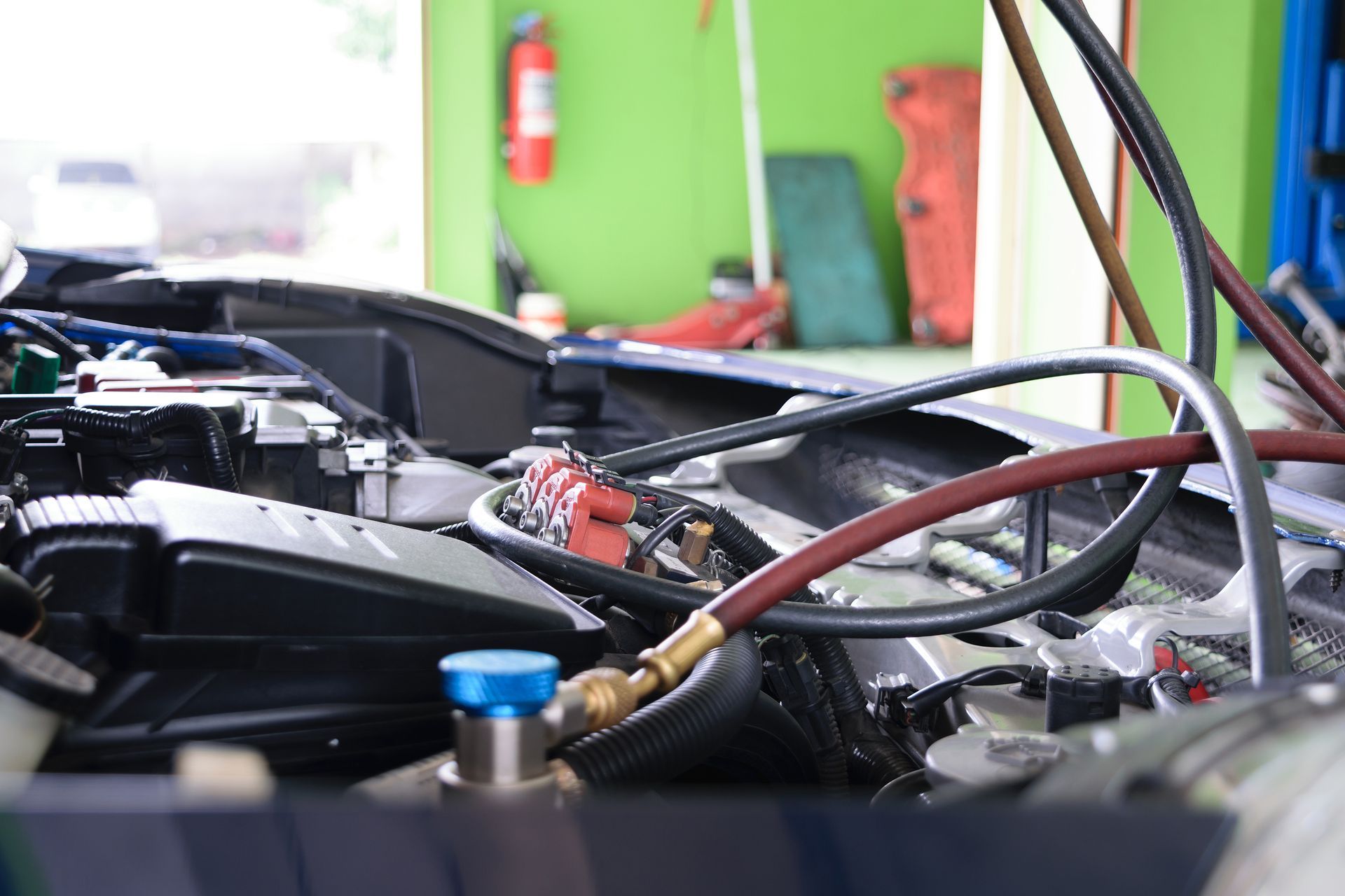 Close-up of an automotive engine bay being serviced with air conditioning manifold gauges in a brightly lit workshop.