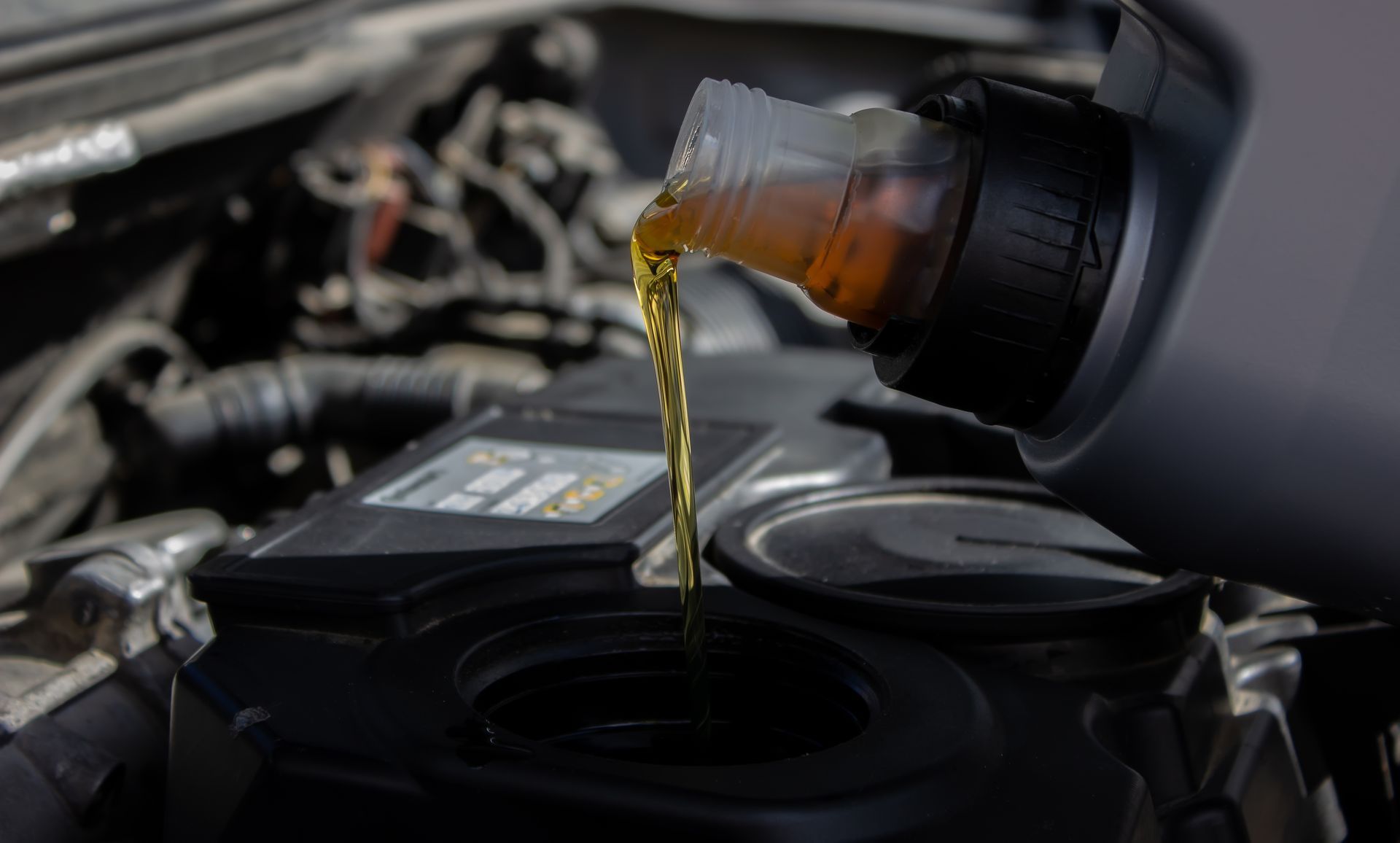 Motor oil being poured into a car engine through the oil filler opening.