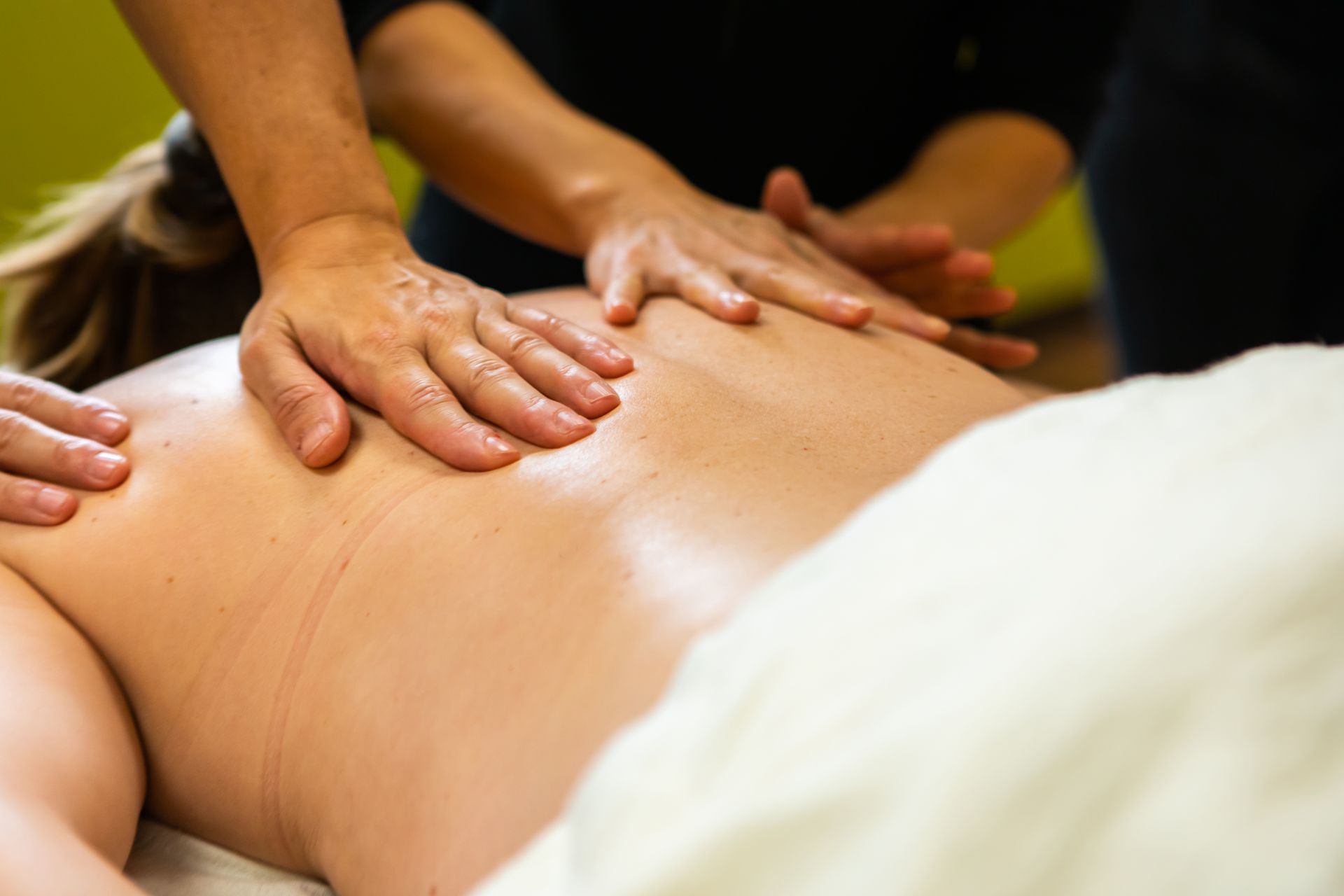 Massage therapist kneading a person’s bare back in a spa setting