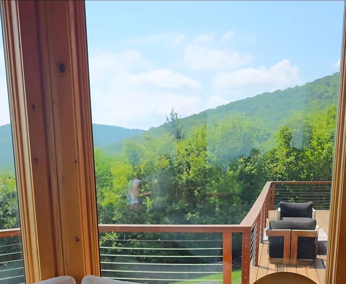 Cozy lounge bed by wooden windows overlooking lush green hills and distant ocean.