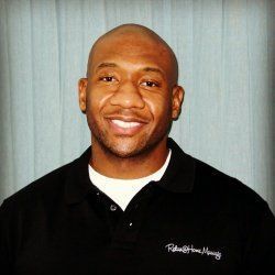 Smiling bald man in a black polo shirt against a light gray curtain backdrop