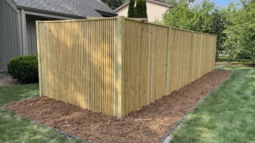 Wooden privacy fence enclosing a side yard beside a house, with mulch along the base and grass beyond.