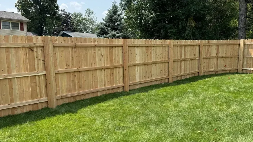 Fresh wooden privacy fence along a green grassy backyard under a partly cloudy sky