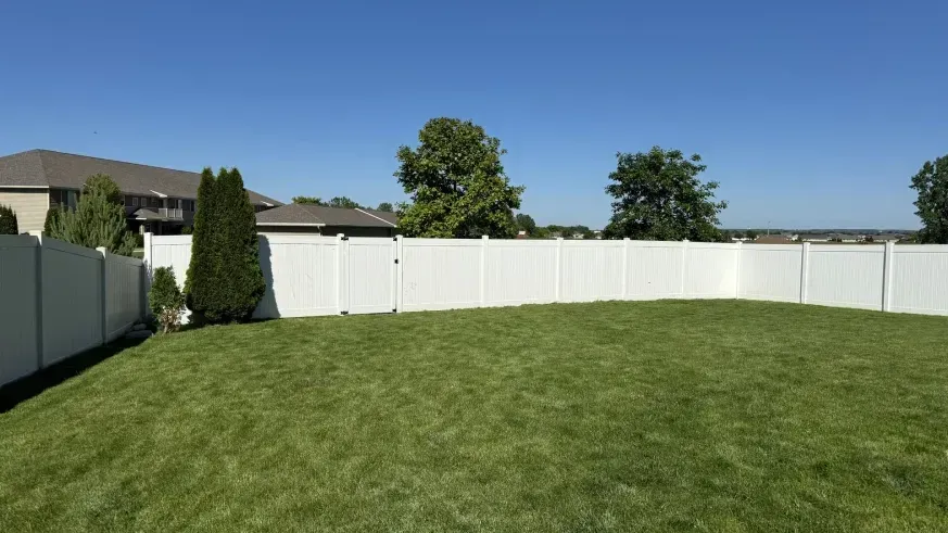 Suburban backyard with a green lawn, white privacy fence, and clear blue sky
