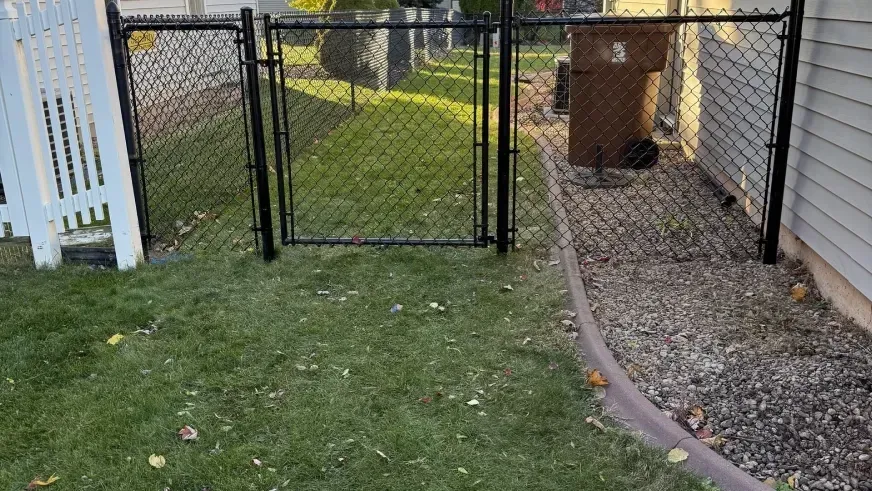 Backyard with open black chain-link gate, green grass, gravel path, and house siding