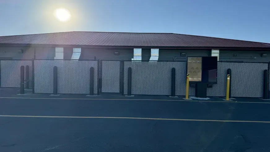 Single-story brick building with a sunlit roof and a parking lot in front.