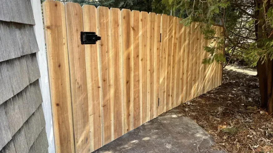 Wooden privacy fence along a concrete path beside a house, with a black latch.