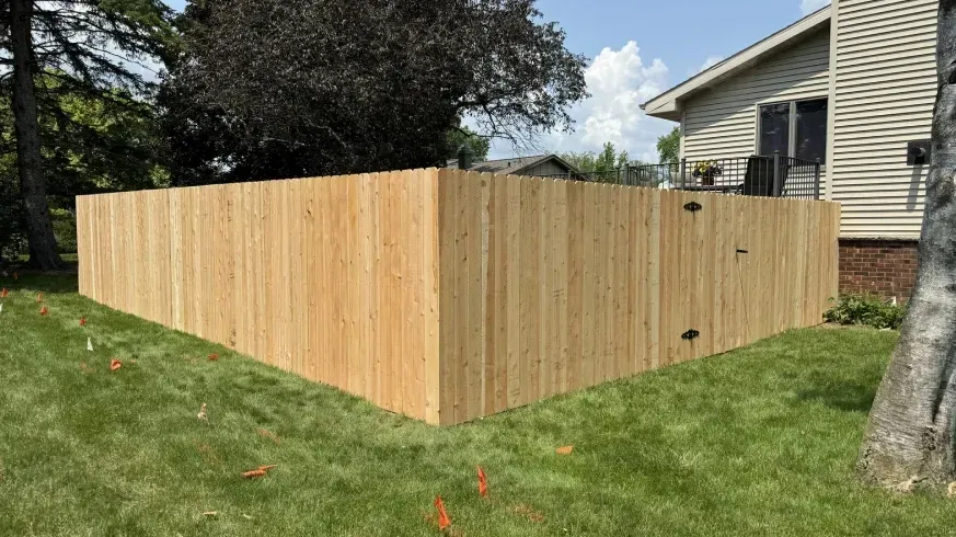 Fresh wood privacy fence enclosing a backyard beside a house with grass and trees