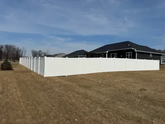 White fence enclosing a dark-roofed house on a grassy lot under a blue sky