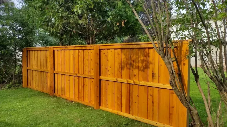 Orange wooden fence along a grassy yard with trees and a white house in the background
