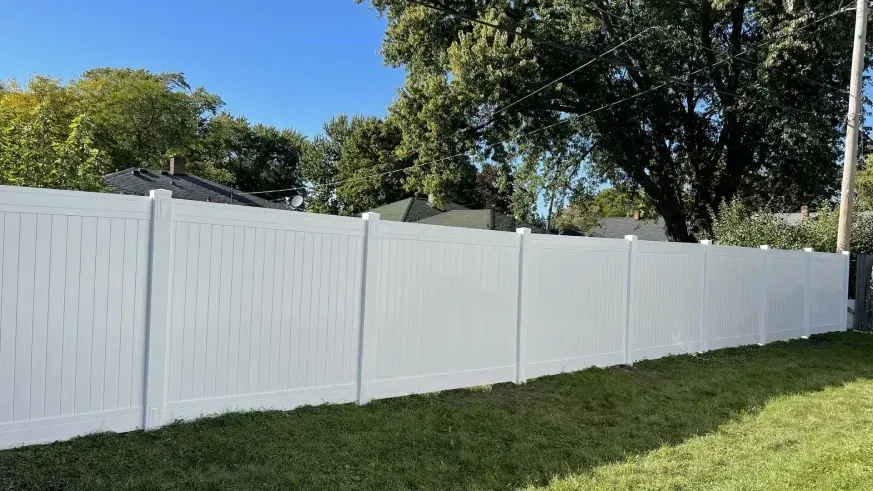 White vinyl fence along a grassy yard with trees and blue sky in the background