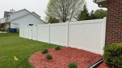 White vinyl fence along a green lawn beside a red brick house and mulch bed with small shrubs