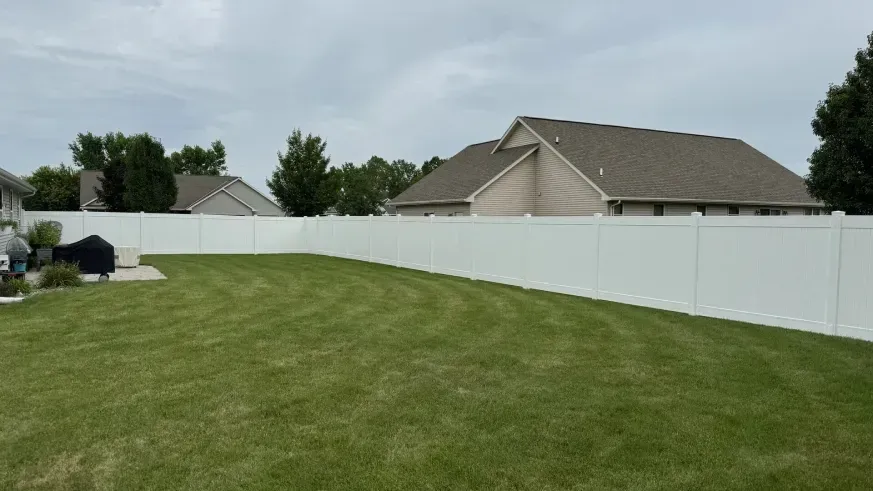 Suburban backyard with a mowed green lawn, white fence, and houses under a cloudy sky