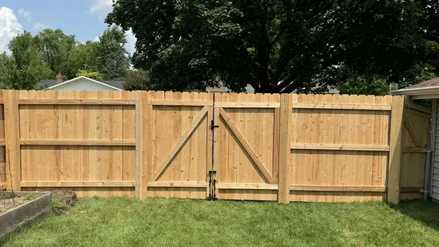 Wooden backyard privacy fence with a central double gate and grass in front.