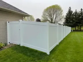 White vinyl privacy fence beside a house, bordering a green lawn and trees