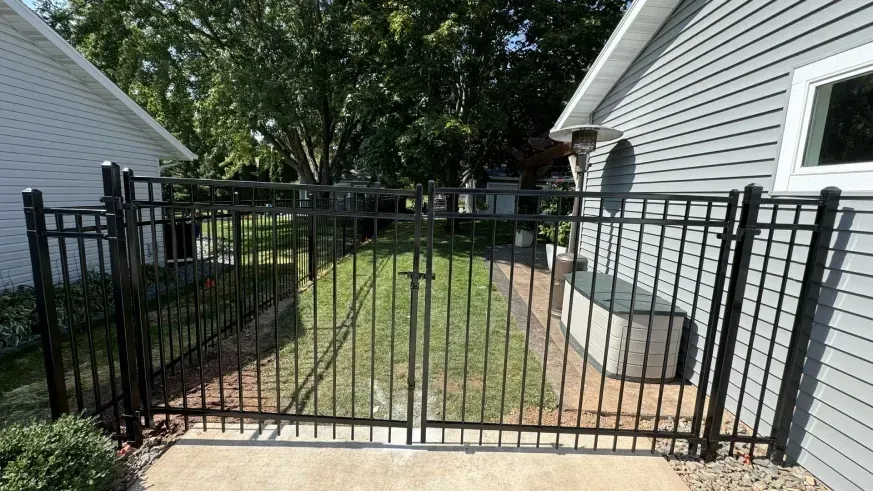 Black metal gate opening onto a narrow grassy side yard between two white houses.
