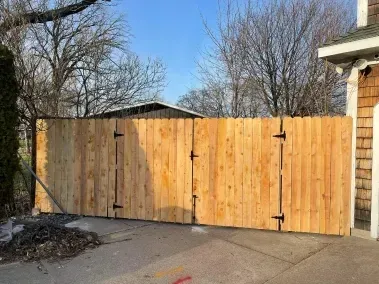 Wooden driveway gate beside a house and leafless trees on a paved driveway