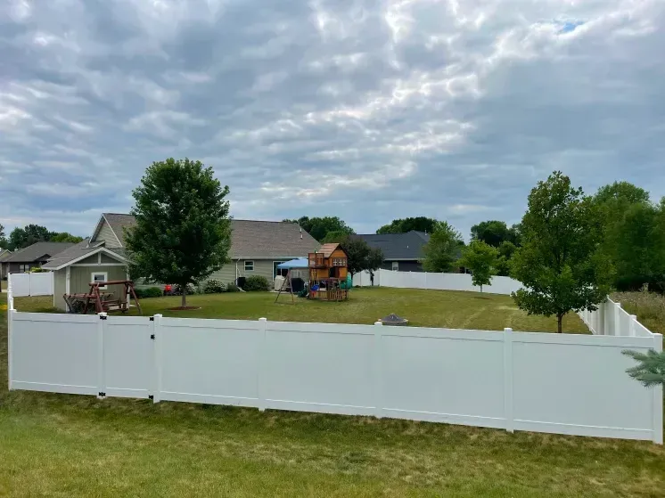 White fenced yard with a house, trees, and a cloudy sky in a suburban neighborhood
