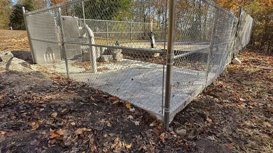 Chain-link fenced outdoor enclosure with a concrete floor in a wooded area.