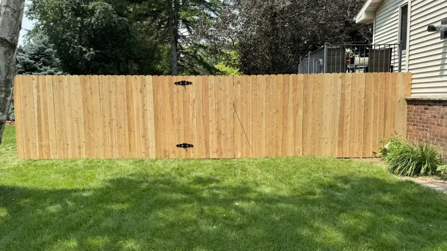 Wooden fence gate in a grassy backyard beside a house and brick wall.