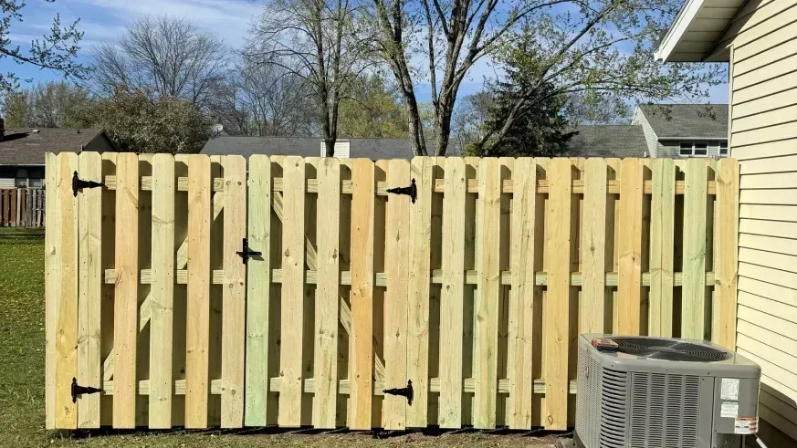 Wooden privacy fence in a backyard beside a beige house, with an air conditioner unit in front.