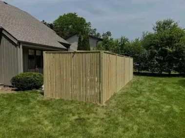 Wooden privacy fence attached to a house beside a grassy backyard lawn