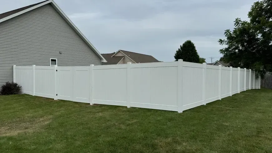 White vinyl privacy fence around a suburban backyard beside a gray house and lawn.